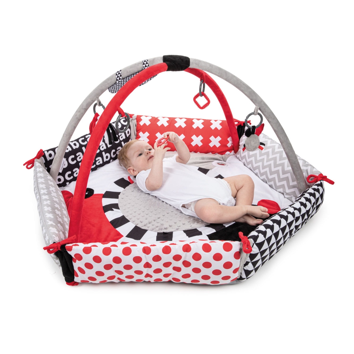 Dziecko leżące na macie Canpol babies SENSORY TOYS z czerwono-szarymi pałąkami i zabawkami rozwijającymi zmysły.