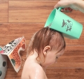 Małe dziecko podczas kąpieli, na głowie spłukiwane włosy wodą z zielonego kubka BabyOno 242 z obrazkiem lisa, chroniącego oczy przed wodą