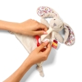 Dwie dłonie trzymają pluszową przytulankę w kształcie króliczka. Osoba zapina zawieszkę na smoczek przy pomocy rzepu babyono 1527 rabbit milly