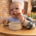 Uśmiechnięte dziecko jedzące przekąskę z silikonowej miseczki Babyono z przyssawką, idealnej do nauki samodzielnego jedzenia